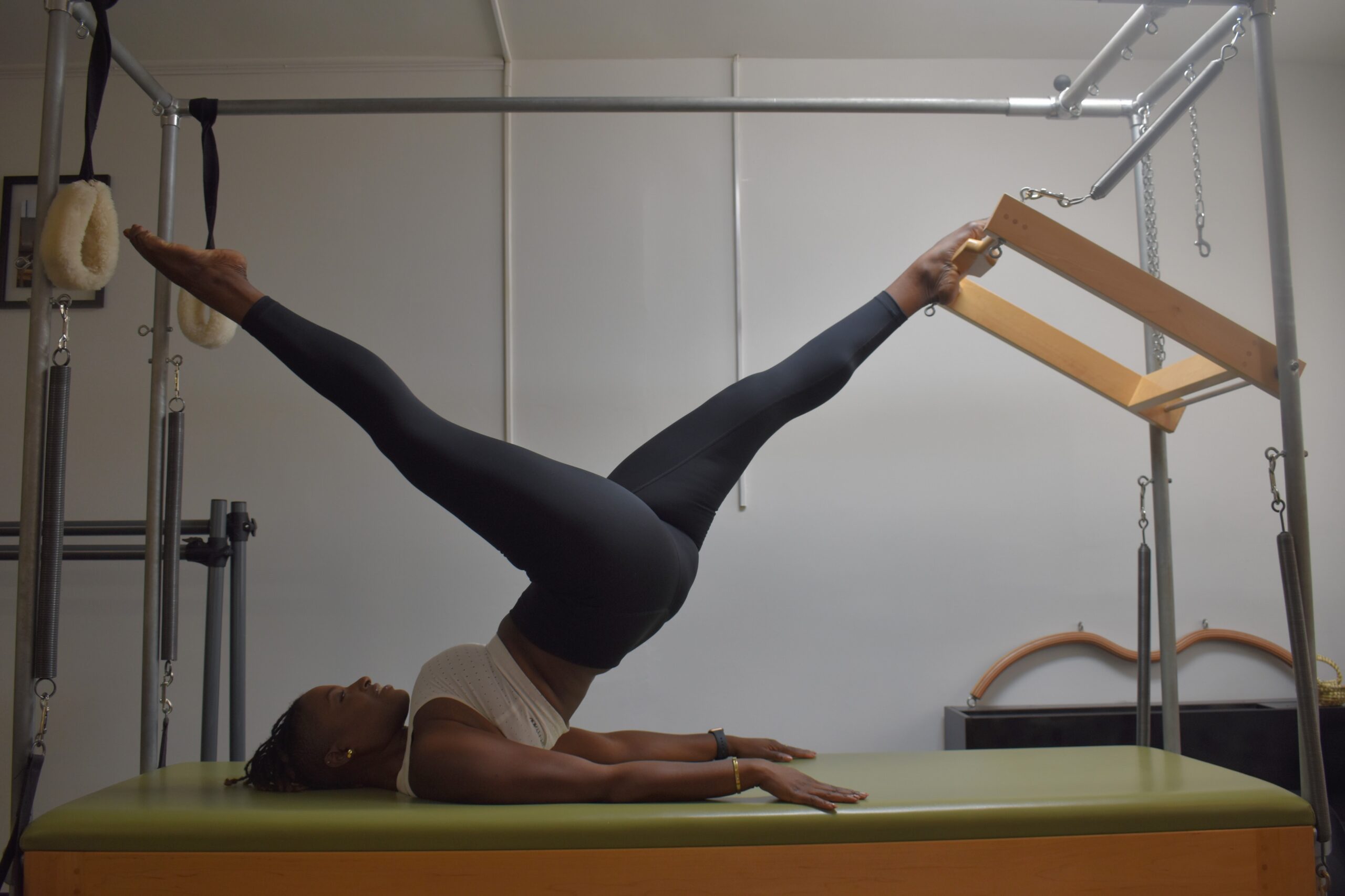 a female dancer on a pilates reformer lifting her hips off the table with her legs in a split