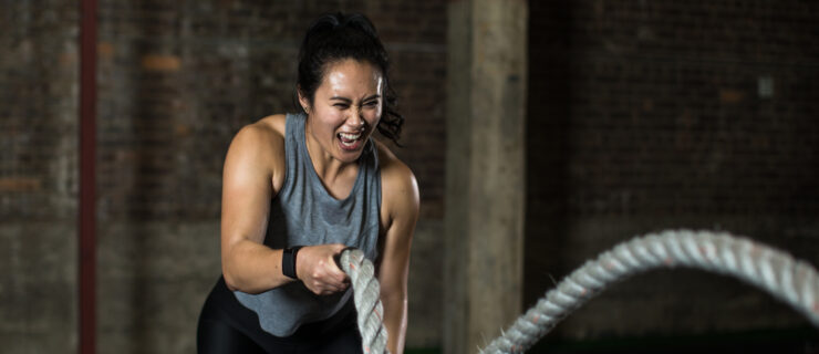 a woman in a grey tank top swinging ropes in both hands